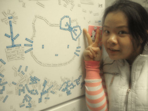 Joii Posing with the Hello Kitty Face Made of Magnets on the Refrigerator